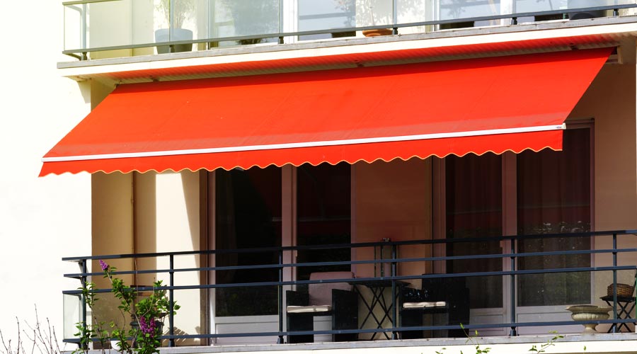 Modelos de cortinas, persianas e toldos: imagem mostra área externa de casa com toldo vermelho, e na parte interna uma cortina ou persiana