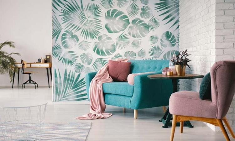 Decoração com papel de parede: a imagem mostra um sofá em frente a um papel de parede estampado com grande folhas de planta.